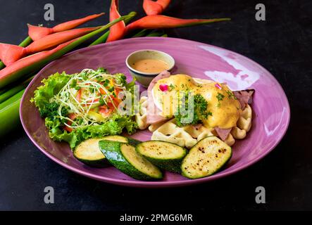 Œufs Benedict (œufs pochés) sur du jambon grillé avec sauce hollande sur des gaufres belges avec courgettes grillées Banque D'Images