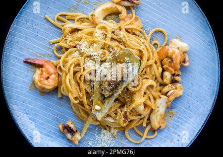 Pâtes carbonara avec fruits de mer sur une assiette bleue avec crevettes isolées sur fond noir vue de dessus Banque D'Images