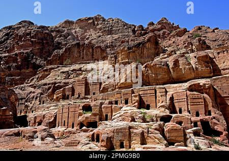 Rue des Façades présentant des rangées de petites tombes nabatéennes taillées dans la roche, creusées dans les immenses falaises de grès sous un ciel bleu clair à Petra, en Jordanie. Banque D'Images
