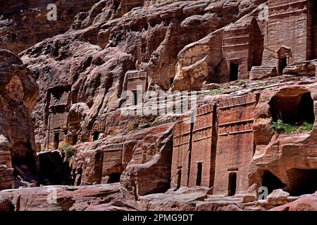 Rue des Façades présentant des rangées de petites tombes nabatéennes taillées dans la roche, creusées dans les immenses falaises de grès sous un ciel bleu clair à Petra, en Jordanie. Banque D'Images