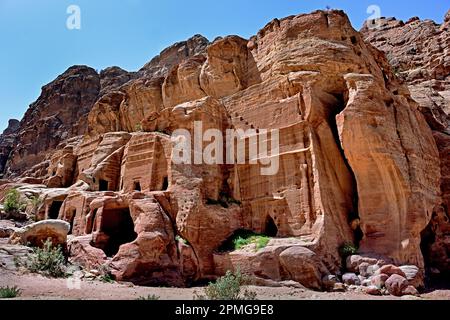 Rue des Façades présentant des rangées de petites tombes nabatéennes taillées dans la roche, creusées dans les immenses falaises de grès sous un ciel bleu clair à Petra, en Jordanie. Banque D'Images