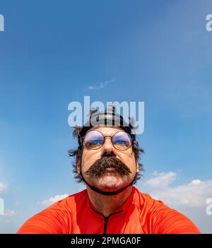 Un cycliste conduit sur un vélo dans un casque rétro sous un ciel bleu Banque D'Images