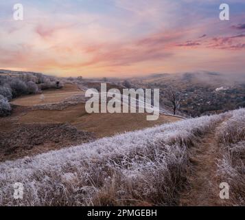 L'hiver approche. Scène pittoresque avant le lever du soleil au-dessus de la fin de l'automne campagne de montagne avec du givre sur les herbes, les arbres, les pentes. Rayons de soleil paisibles f Banque D'Images