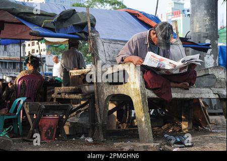 01.08.2013, Yangon, Myanmar, Asie - Un homme est assis sur un banc au bord du fleuve Yangon pour lire un journal. Banque D'Images