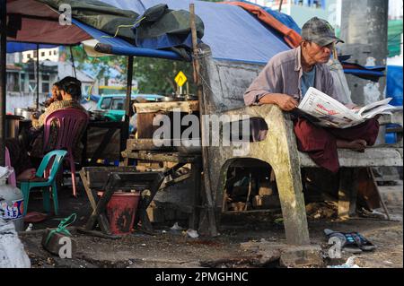 01.08.2013, Yangon, Myanmar, Asie - Un homme est assis sur un banc au bord du fleuve Yangon pour lire un journal. Banque D'Images