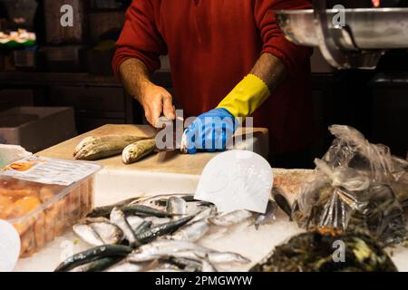Vendeur de poisson non reconnaissable filant un poisson dans un marché, accent sélectif sur le gant bleu et jaune. Banque D'Images
