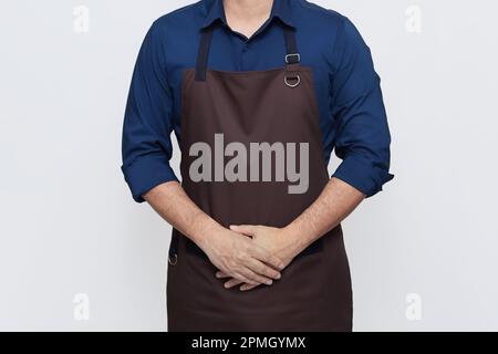 Homme asiatique portant le tablier, un barista ou un chef cuisinier dans des vêtements décontractés et élégants, debout posture d'hospitalité avec les deux mains dans la poche du tablier, pas de visage Banque D'Images