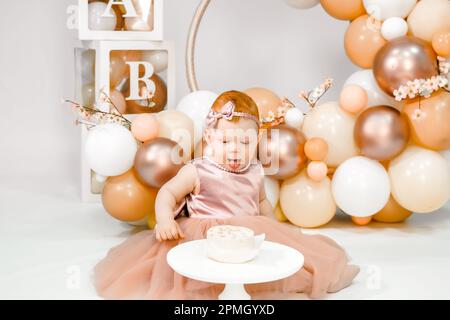 Petite fille à tête rouge fête son premier anniversaire. Cake crash smash, les mains manger. fête de balons familiaux de 1 ans. Séance photo professionnelle. Studio photo Banque D'Images