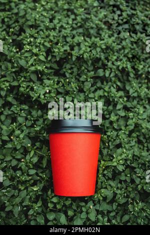 Une tasse de café en papier rouge reposant sur un fond floral vert Banque D'Images