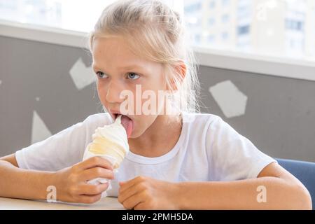 Portrait d'une petite fille drôle et affamée qui mange de la glace froide délicieuse dans une tasse de gaufres assis dans un café. Jour d'été. Un enfant aime la glace. Un suédois Banque D'Images