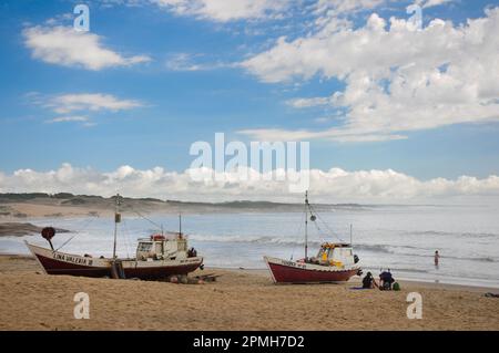 Un couple de bateaux de pêche sur le sable de la plage de Punta del Diablo, tandis qu'une personne repose sur le sable et une autre nage dans la mer Banque D'Images