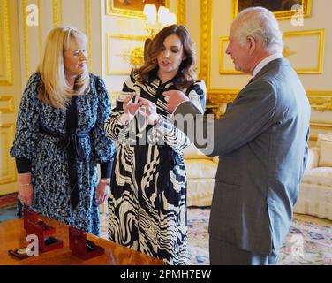 Le roi Charles III reçoit la première pièce de Coronation frappée en £5 par Anne Jessopp, chef de la direction de la monnaie royale (à gauche) et Rebecca Morgan (au centre), au château de Windsor, dans le Berkshire. Un portrait couronné du roi sera pour la première fois sur une nouvelle gamme de pièces commémoratives créées pour célébrer le prochain couronnement. La collection, qui comprend une pièce de 50p et £5, sera libérée plus tard ce mois-ci avant la célébration historique de 6 mai. Date de la photo: Jeudi 13 avril 2023. Banque D'Images