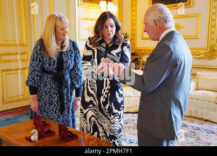 Le roi Charles III reçoit la première pièce de Coronation frappée en £5 par Anne Jessopp, chef de la direction de la monnaie royale (à gauche) et Rebecca Morgan (au centre), au château de Windsor, dans le Berkshire. Un portrait couronné du roi sera pour la première fois sur une nouvelle gamme de pièces commémoratives créées pour célébrer le prochain couronnement. La collection, qui comprend une pièce de 50p et £5, sera libérée plus tard ce mois-ci avant la célébration historique de 6 mai. Date de la photo: Jeudi 13 avril 2023. Banque D'Images