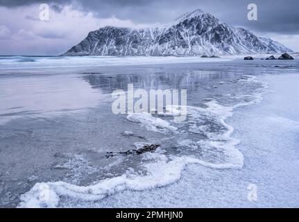 Tracés de vagues gelés sur la plage de Skagsanden, adossée à la montagne d'Hustiden en hiver, près de Flakstad, Flakstadoya, îles Lofoten, comté de Nordland, Norvège, SC Banque D'Images