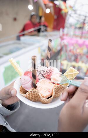 Une jeune femme hispanique mange une glace traditionnelle devant un marché de rue Banque D'Images