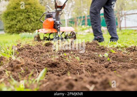 Un homme travaille la terre dans le jardin avec un cultivateur, prépare le sol pour le semis. concept d'agriculture Banque D'Images