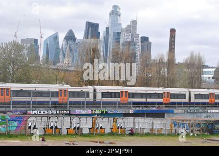 UN ARTISTE GRAFFITI PEINT À SHOREDITCH, DANS L'EST DE LONDRES, AVEC UN TRAIN HORS-TERRAIN QUI PASSE ET UNE VUE SUR LA VILLE DE LONDRES AU-DELÀ DE LUI. Banque D'Images