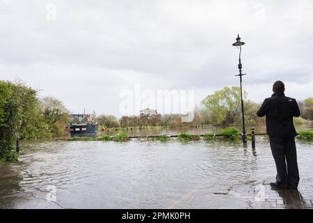 Un homme debout sur un terrain plus élevé arpentant une péniche et un poste de lampe submergé dans le centre commercial Chiswick à Chiswick, dans le sud-ouest de Londres, en Angleterre, au Royaume-Uni Banque D'Images