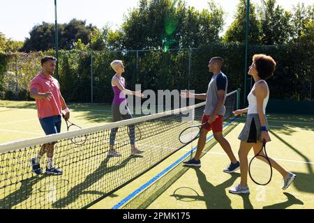 Joyeux groupe diversifié d'amis jouant au tennis, se serrant la main sur le court de tennis Banque D'Images