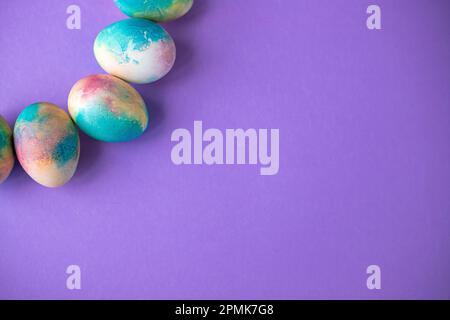 Composition de Pâques avec œufs colorés dans un panier, lapin en bois et fleurs printanières sur fond violet. Cadre de Pâques d'oeufs peints en violet c Banque D'Images