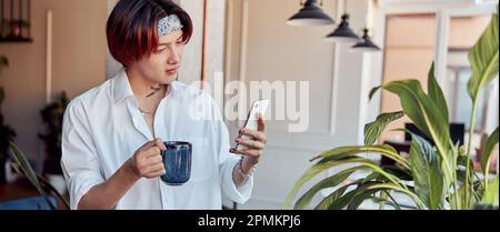 Homme asiatique élégant prenant une photo d'une plante et tenant une tasse de café Banque D'Images