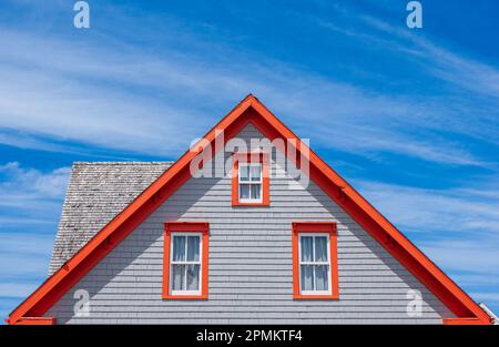 Habitation à pignons latéraux avec revêtement en bardeaux gris. L'orange est utilisé comme couleur d'accentuation sur les garnitures et les bordures de toit, ce qui les fait éclater contre le ciel bleu. Banque D'Images