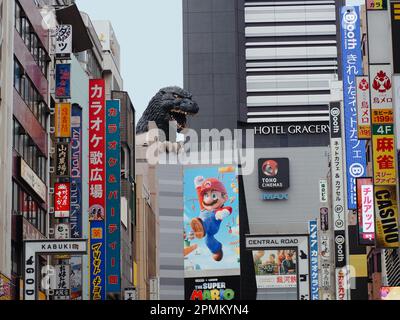 TOKYO, JAPON - 12 avril 2023: Statue de Godzilla sur un cinéma Toho à Shinjuku qui a une affiche pour le Super Mario Bros. Film sur elle. Banque D'Images