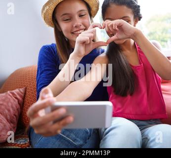 Bestie amour. deux amis adolescents prenant un selfie tout en faisant une forme de coeur avec leurs mains. Banque D'Images