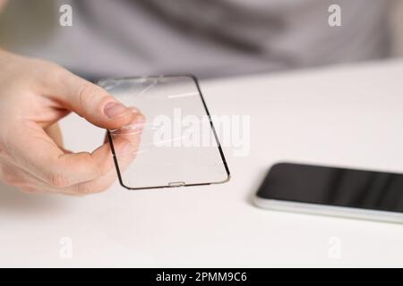 L'homme retire l'ancien verre de protection fissuré du téléphone. Verre de protection cassé Banque D'Images