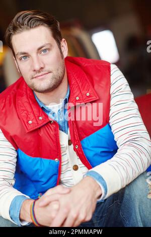 Portrait d'un homme tendance dans une veste rétro lumineuse assise dans un magasin de mode. Jeune homme attrayant porter décontracté élégant vintage rouge et bleu Banque D'Images