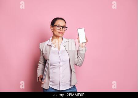 Femme d'affaires enceinte femme à lunettes, portant un ordinateur portable et montrant un smartphone avec écran numérique blanc. Maquette Banque D'Images