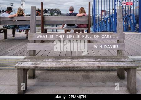 Banc en bois avec citation inspirante de W.H. Davies au bord de l'eau du port de Whitstable, côte nord du Kent, Angleterre, Royaume-Uni. Banque D'Images