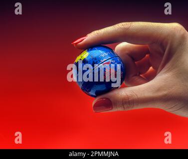 1991 MAIN DE FEMME HISTORIQUE TENANT LE GLOBE TERRESTRE DE PLANÈTE JOUET SUR FOND ROUGE Banque D'Images