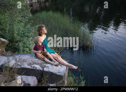 une adolescente de 16 ans et un garçon de 5 ans (frère et sœur) sont heureux de s'asseoir ensemble sur un rocher près du lac et de fantasmer avec de l'int Banque D'Images