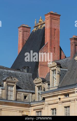 Palais de Fontainebleau : cheminées en briques, toit en tuiles d'ardoise à pente abrupte et acroterie d'or au sommet du monument médiéval de la place de la Fontaine Banque D'Images