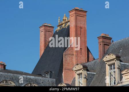 Palais de Fontainebleau : cheminées en briques, toit en tuiles d'ardoise à pente abrupte et acroterie d'or au sommet du monument médiéval de la place de la Fontaine Banque D'Images