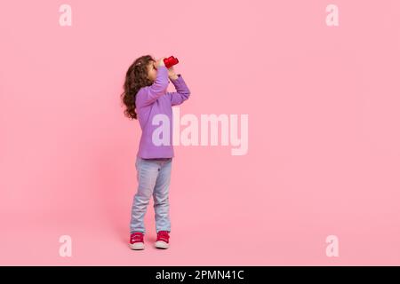 Pleine photo de funky dreamy petit enfant porter violet chandail regardant jumelles espace vide isolé couleur rose fond Banque D'Images