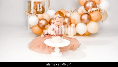 Petite fille à tête rouge fête son premier anniversaire. Cake crash smash, les mains manger. fête de balons familiaux de 1 ans. Séance photo professionnelle. Studio photo Banque D'Images