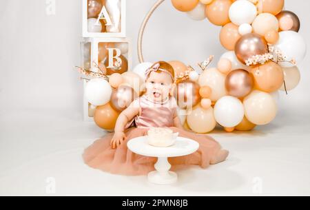 Petite fille à tête rouge fête son premier anniversaire. Cake crash smash, les mains manger. fête de balons familiaux de 1 ans. Séance photo professionnelle. Studio photo Banque D'Images