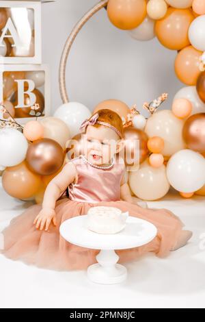 Petite fille à tête rouge fête son premier anniversaire. Cake crash smash, les mains manger. fête de balons familiaux de 1 ans. Séance photo professionnelle. Studio photo Banque D'Images