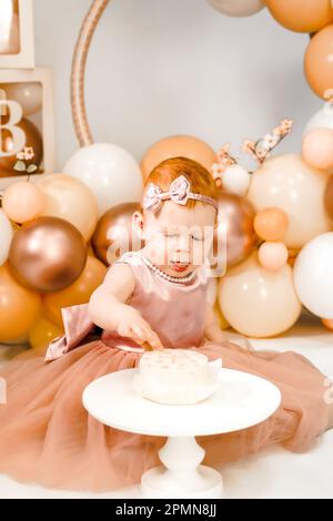 Petite fille à tête rouge fête son premier anniversaire. Cake crash smash, les mains manger. fête de balons familiaux de 1 ans. Séance photo professionnelle. Studio photo Banque D'Images