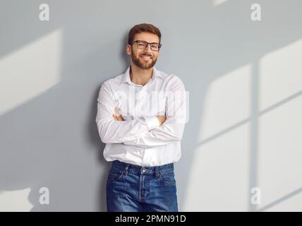 Homme barbu souriant dans des lunettes posant avec des bras croisés Banque D'Images
