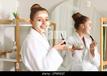 Jeune femme avec masque curcuma et brosse dans la salle de bains Banque D'Images