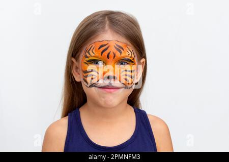 Portrait d'une jeune fille caucasienne souriante de six ans regardant l'appareil photo sur fond blanc avec la peinture de visage de tigre Banque D'Images