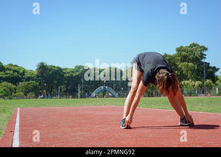 jeune latina femme d'origine argentine s'étirant sur la piste de course, debout et penchée vers l'avant en touchant ses pieds avec ses mains, entrainement g. Banque D'Images