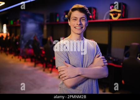 Portrait de jeune joueur positif posant et regardant la caméra dans le cyber club, image de stock Banque D'Images