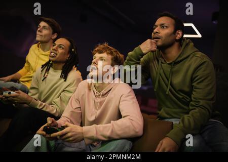 KIEV, UKRAINE - 13 FÉVRIER 2023: L'homme indien concentré assis près d'amis multiethniques jouant le jeu vidéo dans le cyber club, image de stock Banque D'Images