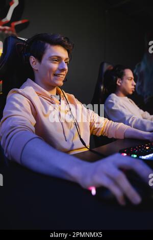 Joueur souriant avec casque assis près du clavier dans le cyber club, image de stock Banque D'Images