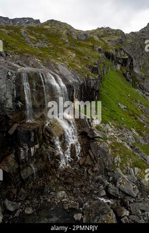 Reed Falls, une chute d'eau glaciaire coulant sur l'herbe couverte, rocheuse à flanc de montagne à Archange Hatcher Pass sous un ciel gris et nuageux près d'Independent... Banque D'Images