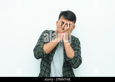 Le jeune homme asiatique couvre son visage avec des paumes avec des yeux légèrement peeking Banque D'Images